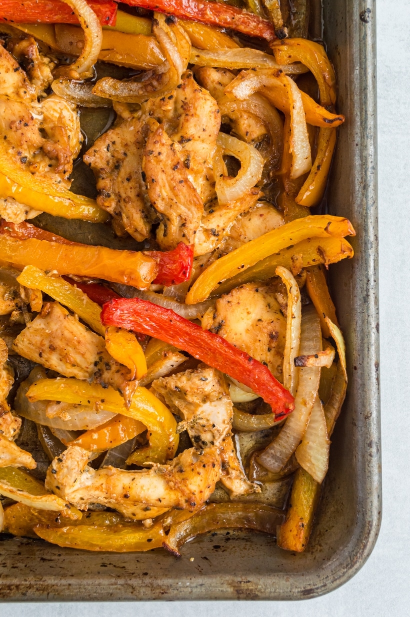 Broiled Sheet Pan Chicken Fajitas A detailed close-up of roasted chicken fajitas on a sheet pan with bell peppers, and onions with a slight char from the broiler.