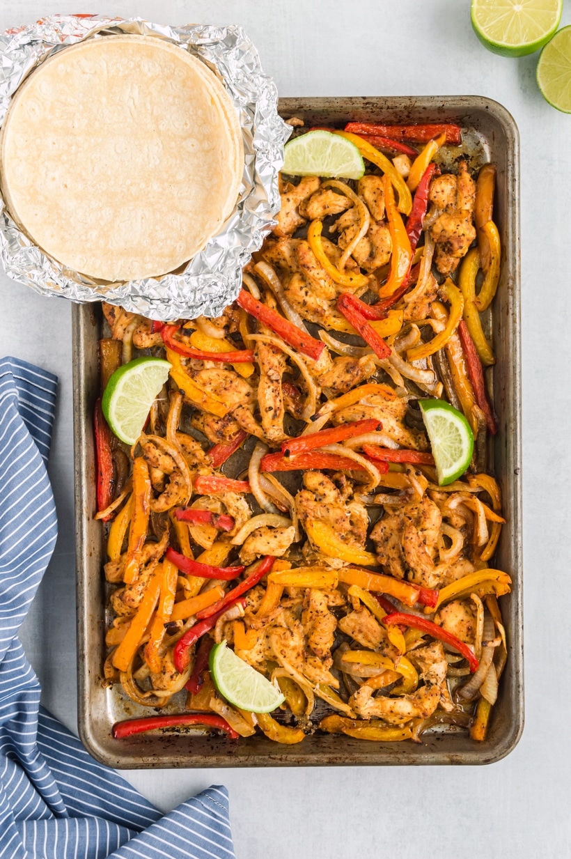 Sheet Pan Chicken Fajitas with homemade corn tortillas A pan of freshly baked chicken fajitas with warm tortillas placed beside it, ready for serving.