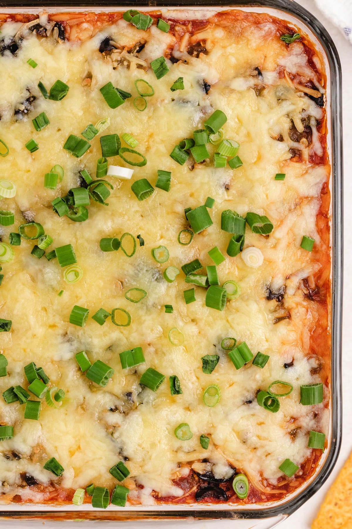 Overhead view of a cheesy baked taco dip with a golden crust, garnished with fresh green onions.