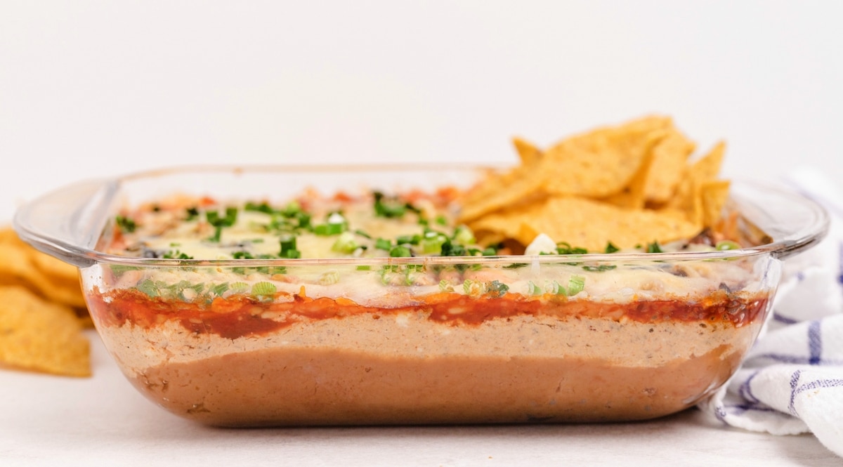 Close-up overhead shot of the layered taco dip in a baking dish, showing refried beans, chili, and salsa.