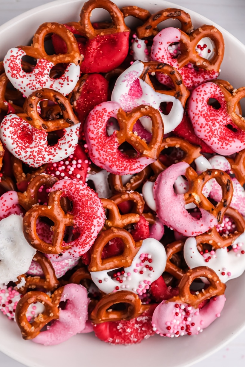 A close-up of Cupid’s Pretzel Treats on a parchment-lined baking sheet, coated in pink, red, and white candy melts with festive sprinkles.