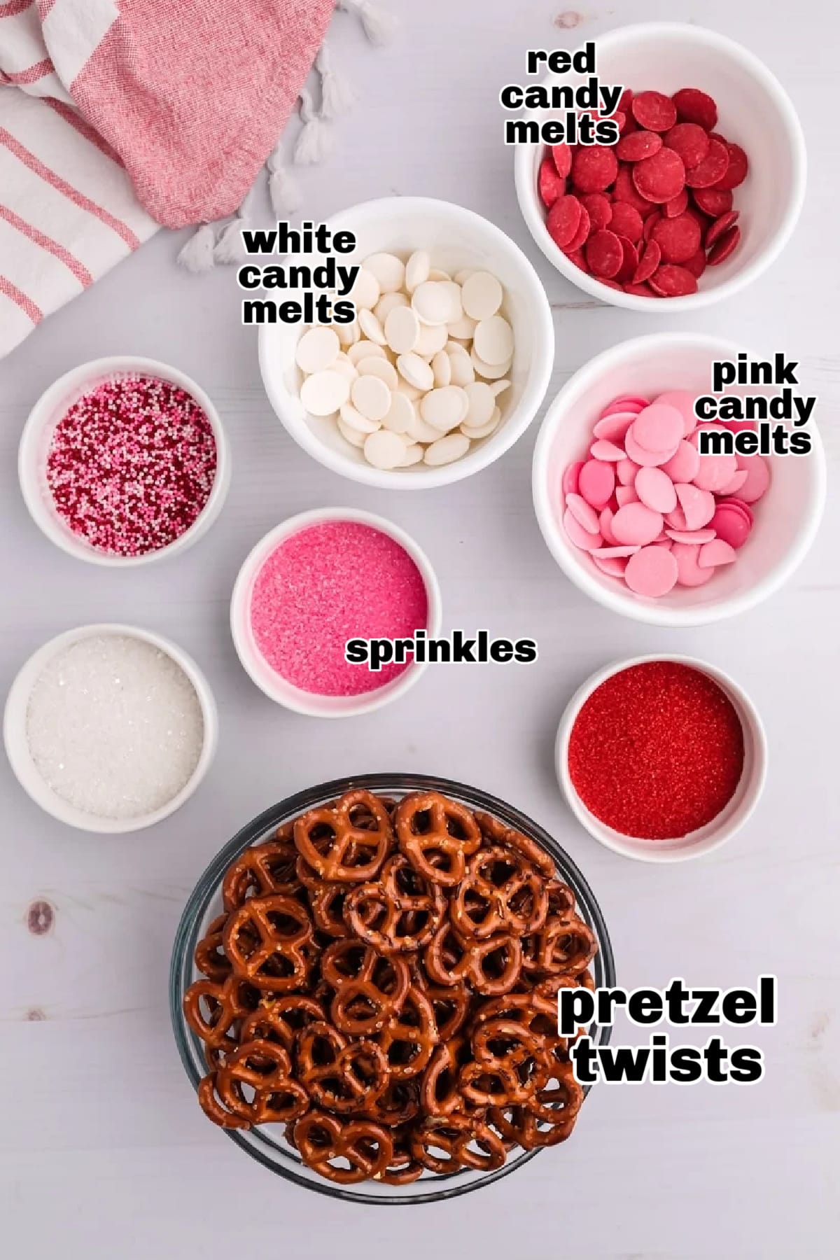 A flat lay of ingredients, including mini pretzels, candy melts, and sprinkles, arranged on a countertop.