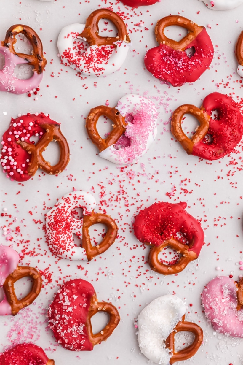 A handful of decorated Cupid's pretzel treats placed on the counter with sprinkles for Valentine's Day.