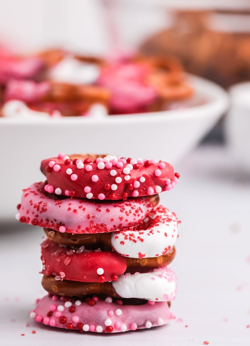 A stack of Valentine's Day Cupid's pretzel tretas on a plate, highlighting the glossy candy coating and sprinkles.