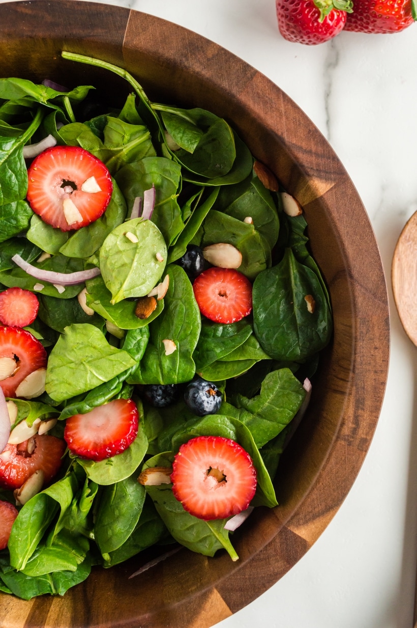 Strawberry Spinach Salad with Strawberry Vinaigrette in a bowl Overhead view of a fully prepared Strawberry Spinach Salad in a wooden bowl, showcasing fresh strawberries, spinach, almonds, and red onion.