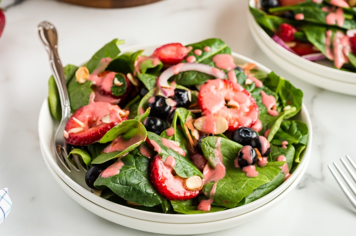 Strawberry Spinach Salad with Strawberry Vinaigrette being served Side view of Strawberry Spinach Salad with vinaigrette drizzled on top, highlighting the vibrant colors and textures of the ingredients.