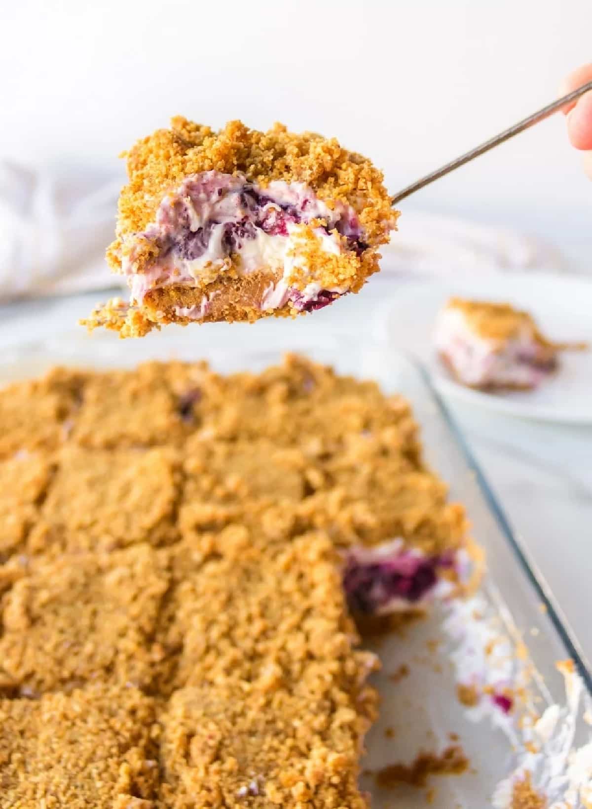 Slice of Blueberry Cheesecake Icebox Cake held over baking dish A slice of blueberry cheesecake icebox cake lifted on a spatula above the full pan