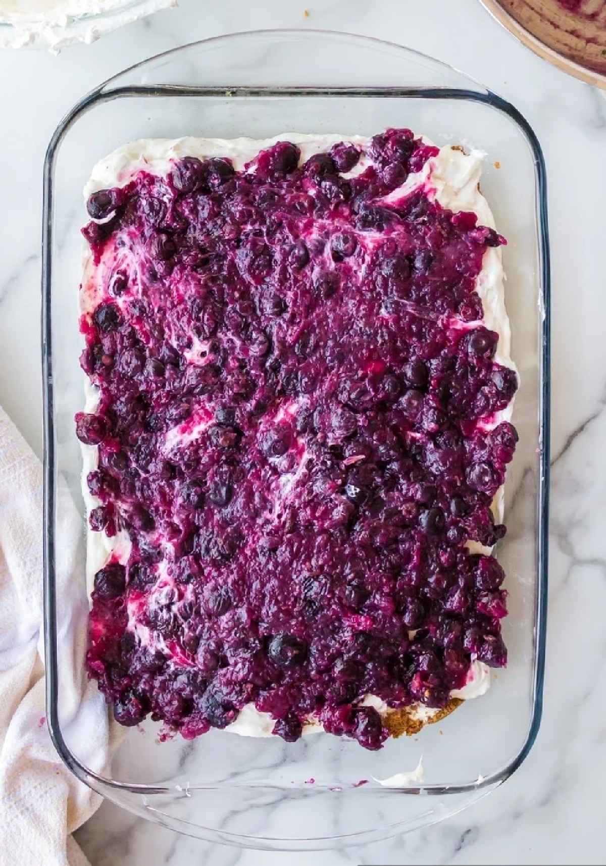 Adding blueberry topping to Blueberry Cheesecake Icebox Cake Blueberry topping spread over cream cheese layer during cake assembly