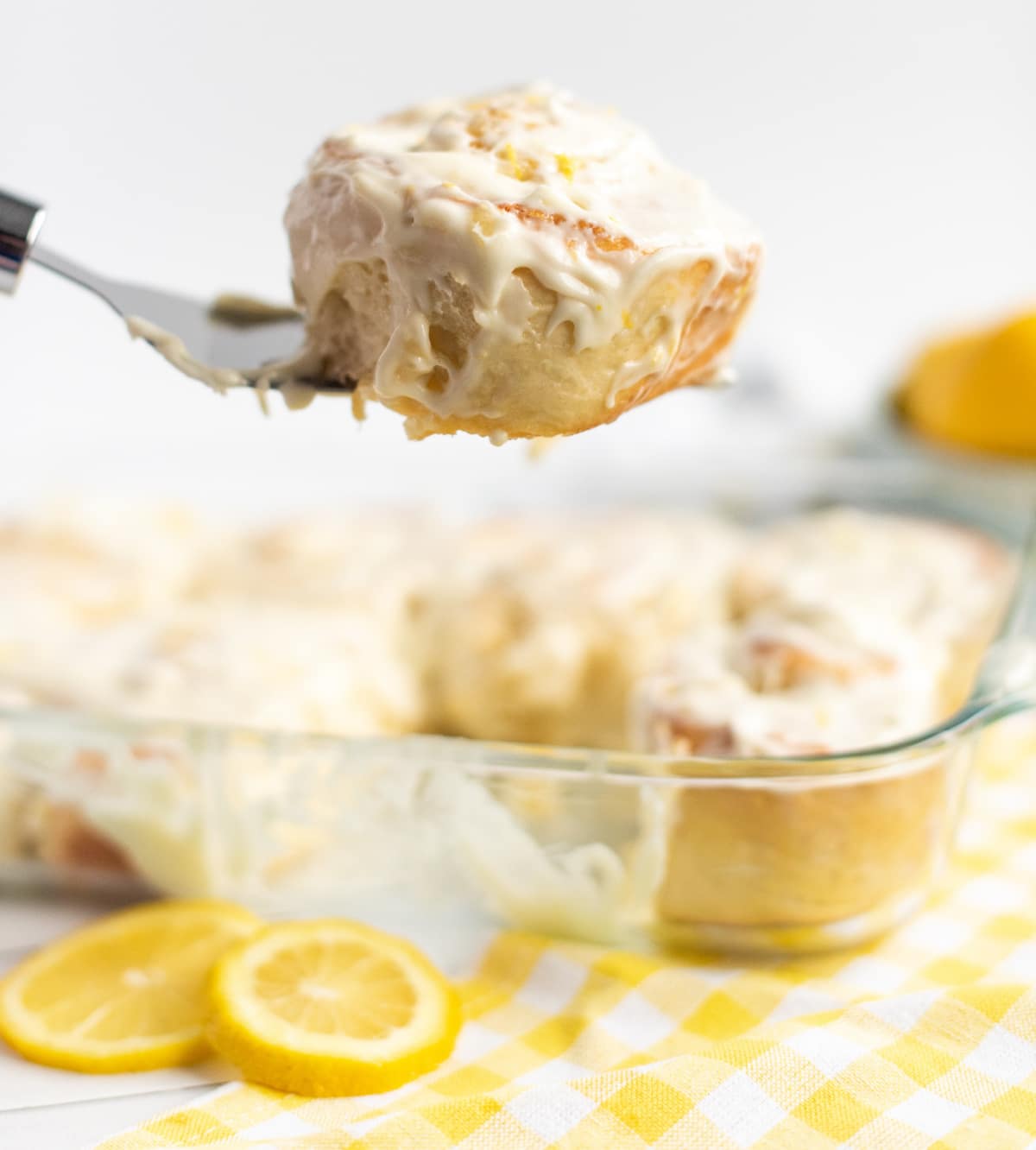 Lemon Buns with Lemon Cream Cheese Icing A spatula lifting a lemon bun from the baking dish, showing its soft texture and layers of filling.