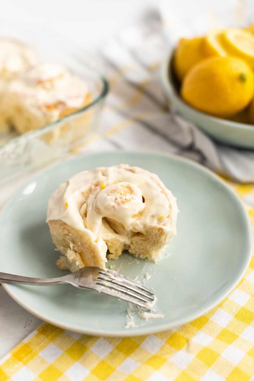 Lemon Buns with Lemon Cream Cheese Icing ready to serve A single lemon bun served on a blue plate, generously topped with lemon cream cheese icing.