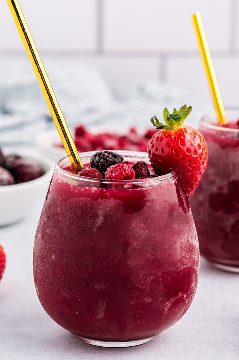 Side view of red wine slushie in stemless glass with strawberry and gold straw