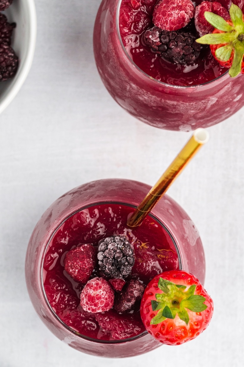 Overhead shot of red wine slushie in glass with frozen berries and gold straw