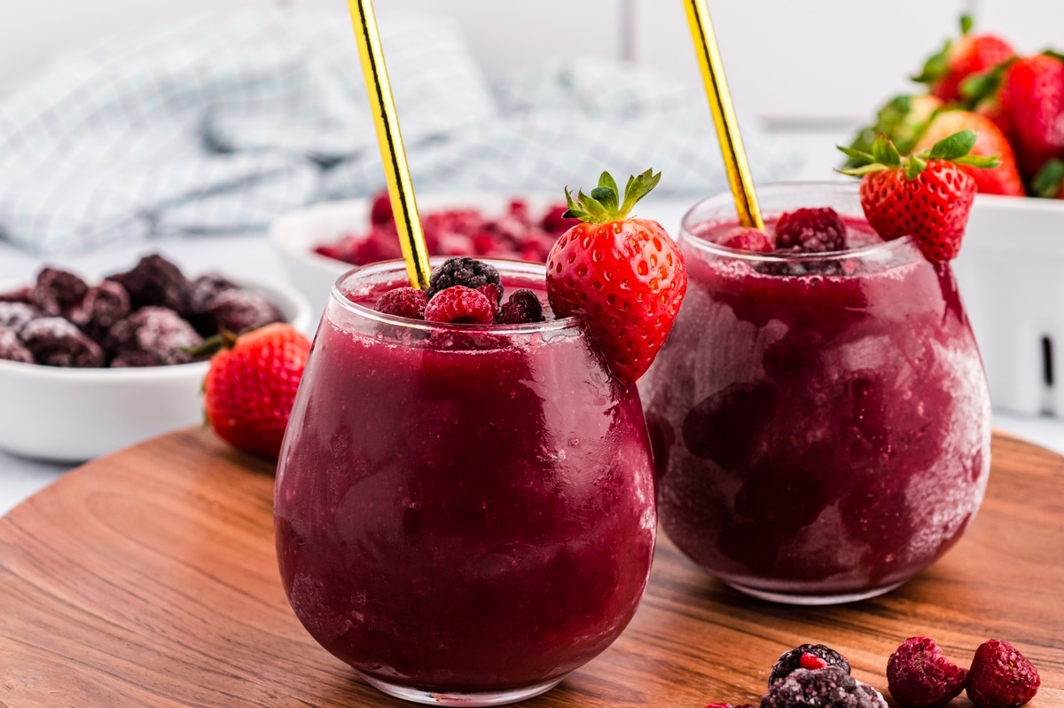 Two glasses of wine slushie on a table with frozen berries around