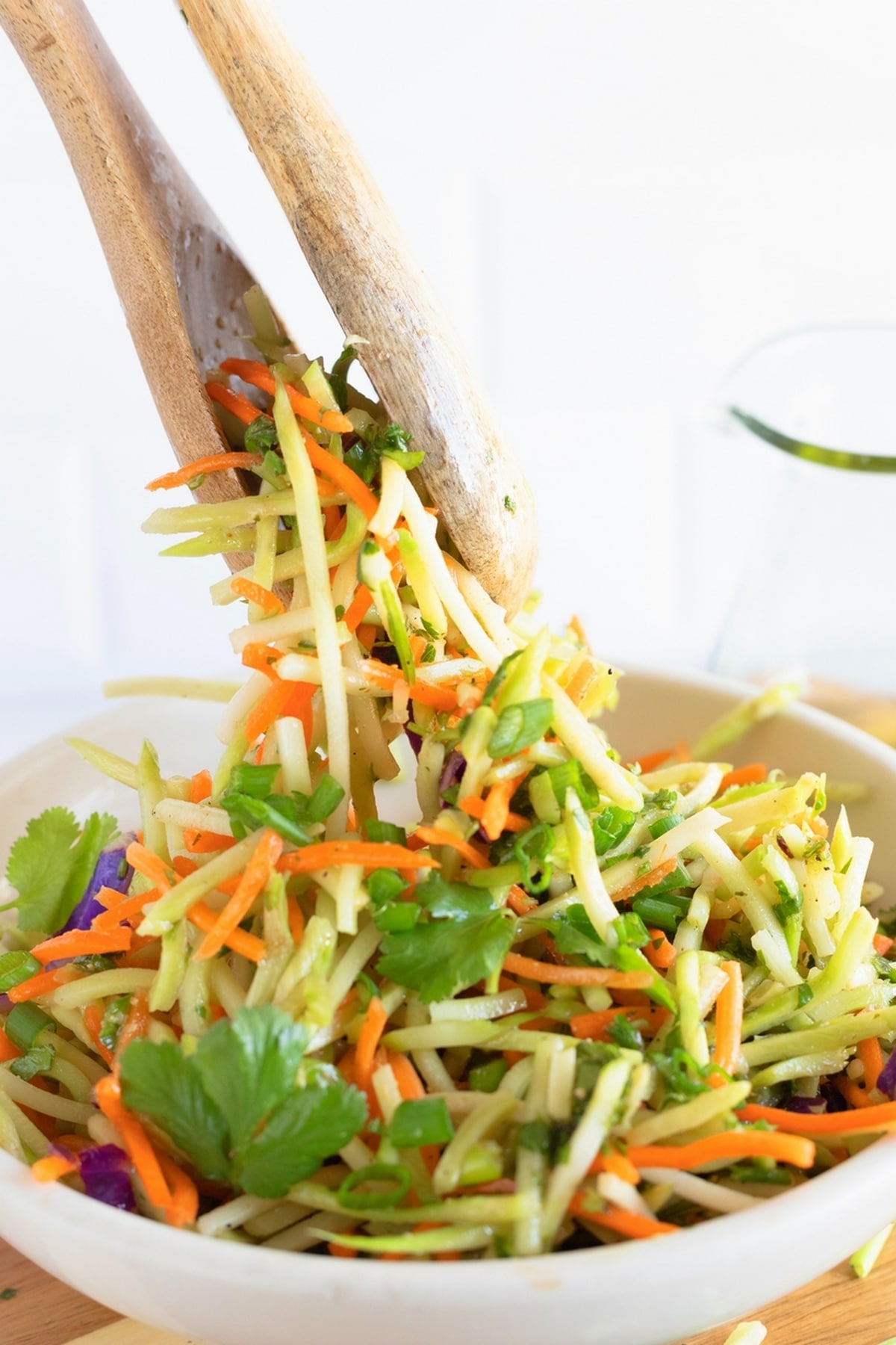 Cilantro Lime Broccoli Slaw with wooden spoons. Hand tossing cilantro lime broccoli slaw with dressing in a large bowl.