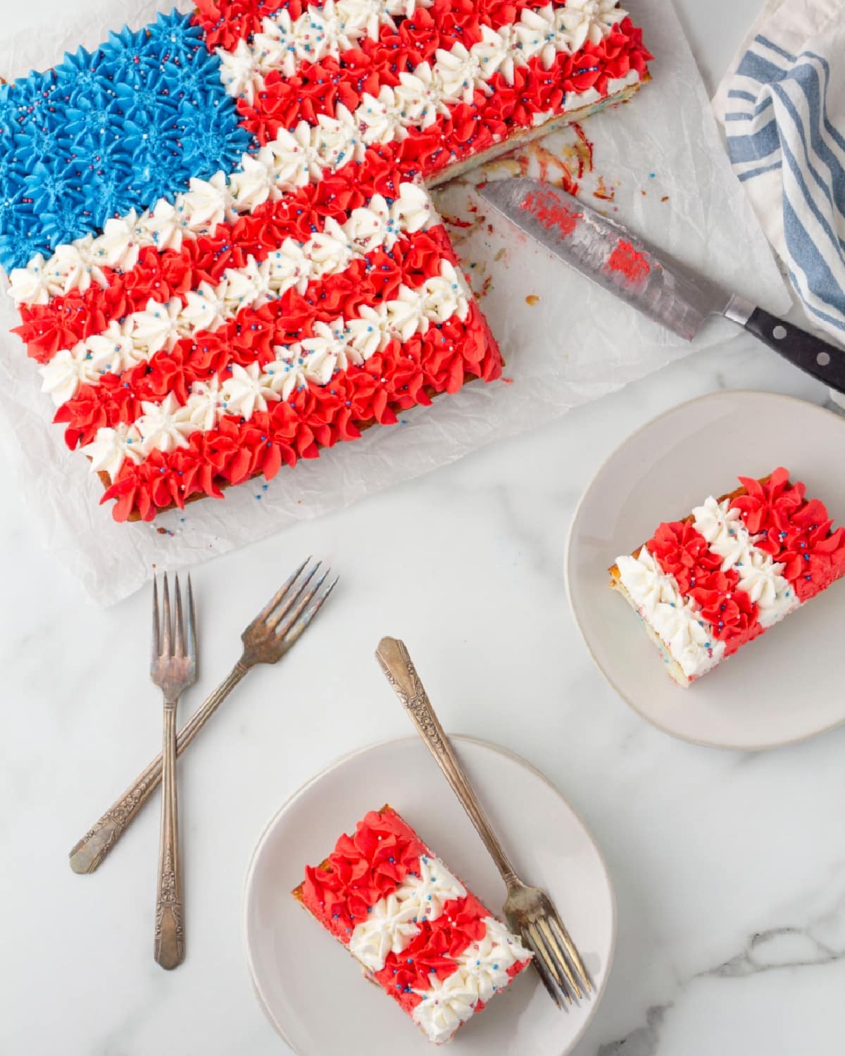 Overhead of buttercream flag cake with piped star pattern, one slice removed and plated with forks.