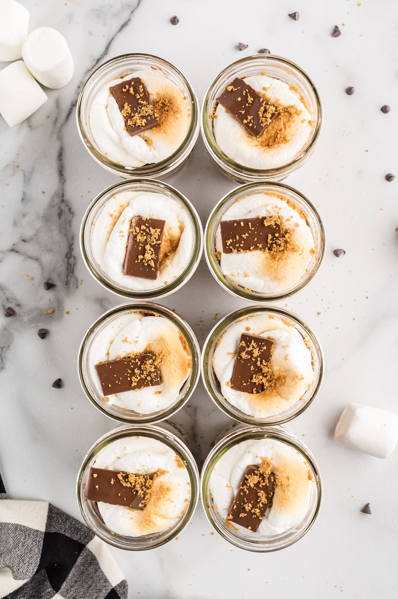 Top-down view of eight s’mores pudding parfaits in jars, each topped with toasted marshmallow and chocolate