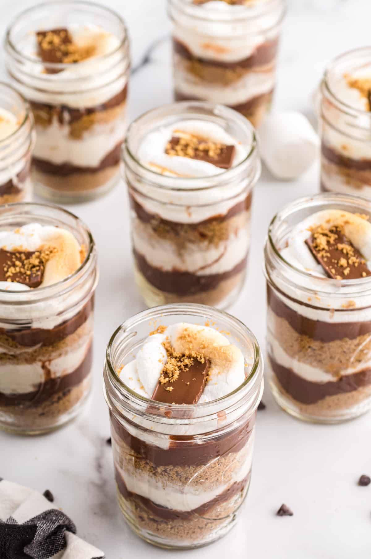 Overhead of s’mores parfait ingredients including pudding mix, graham crumbs, chocolate chips, and marshmallows