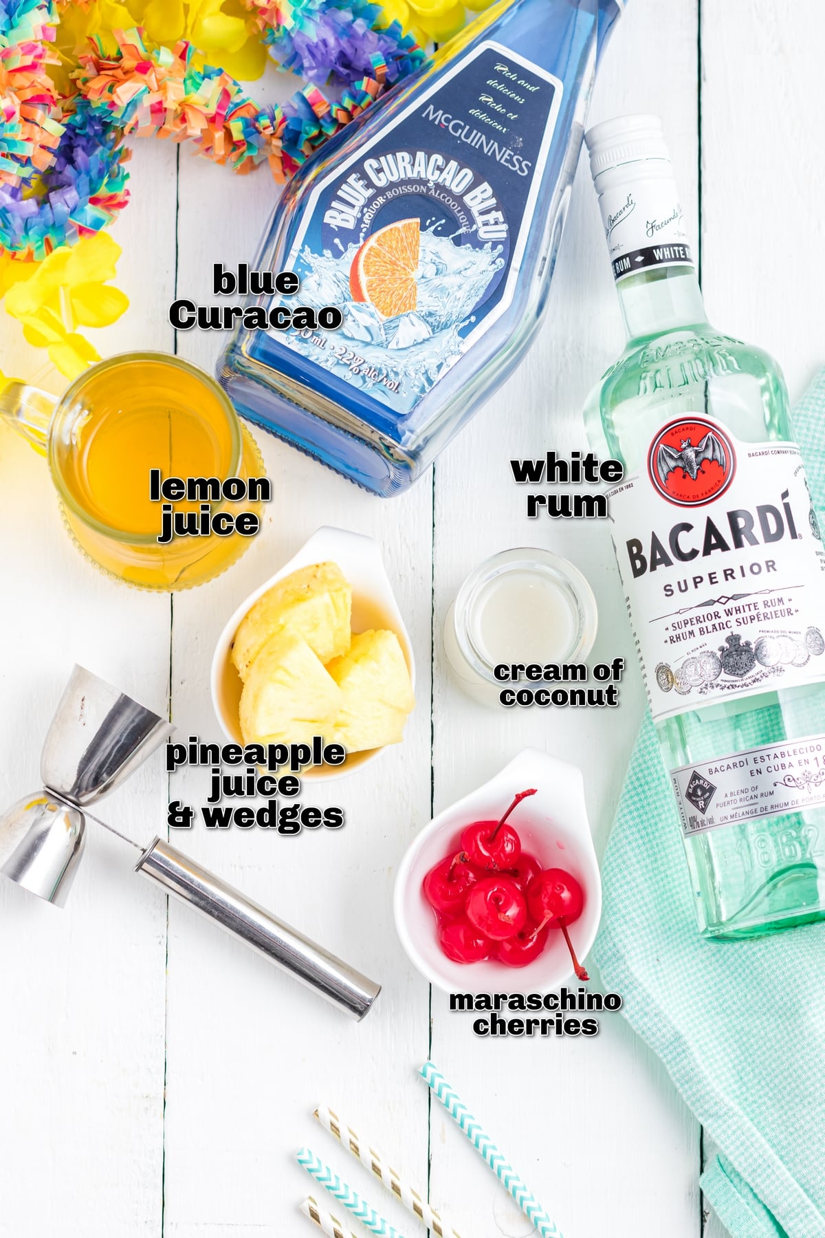 This Blue Hawaiian cocktail tastes like a vacation in a glass. Notes of pineapple, coconut and citrus from the Blue Curacao liqueur make it the perfect tropical cocktail for summer parties! ingredients for a blue Hawaiian cocktail laid out on a countertop including rum, pineapple juice, cream of coconut and blue curacao