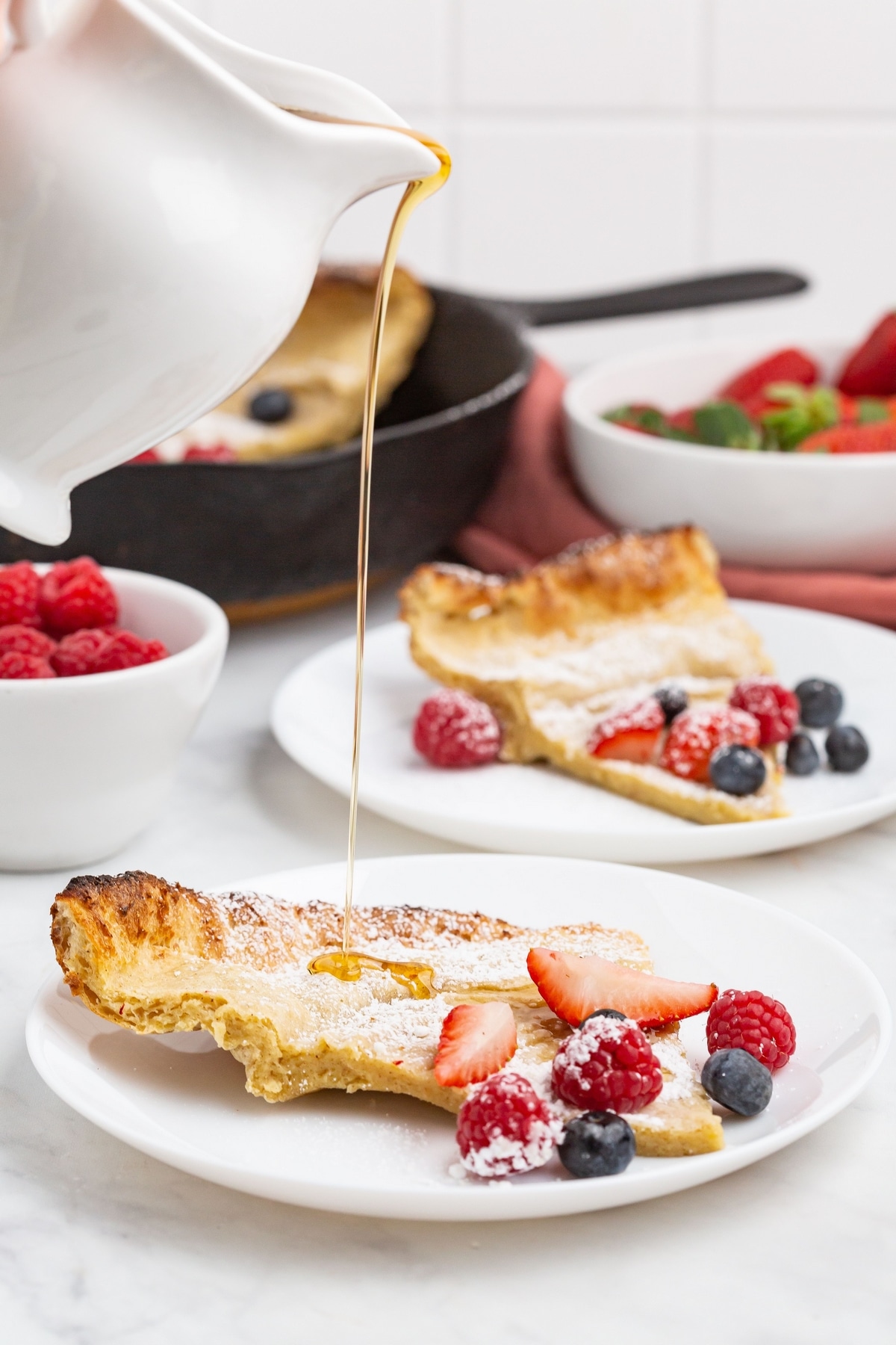 Syrup being poured onto a slice of Dutch baby pancake