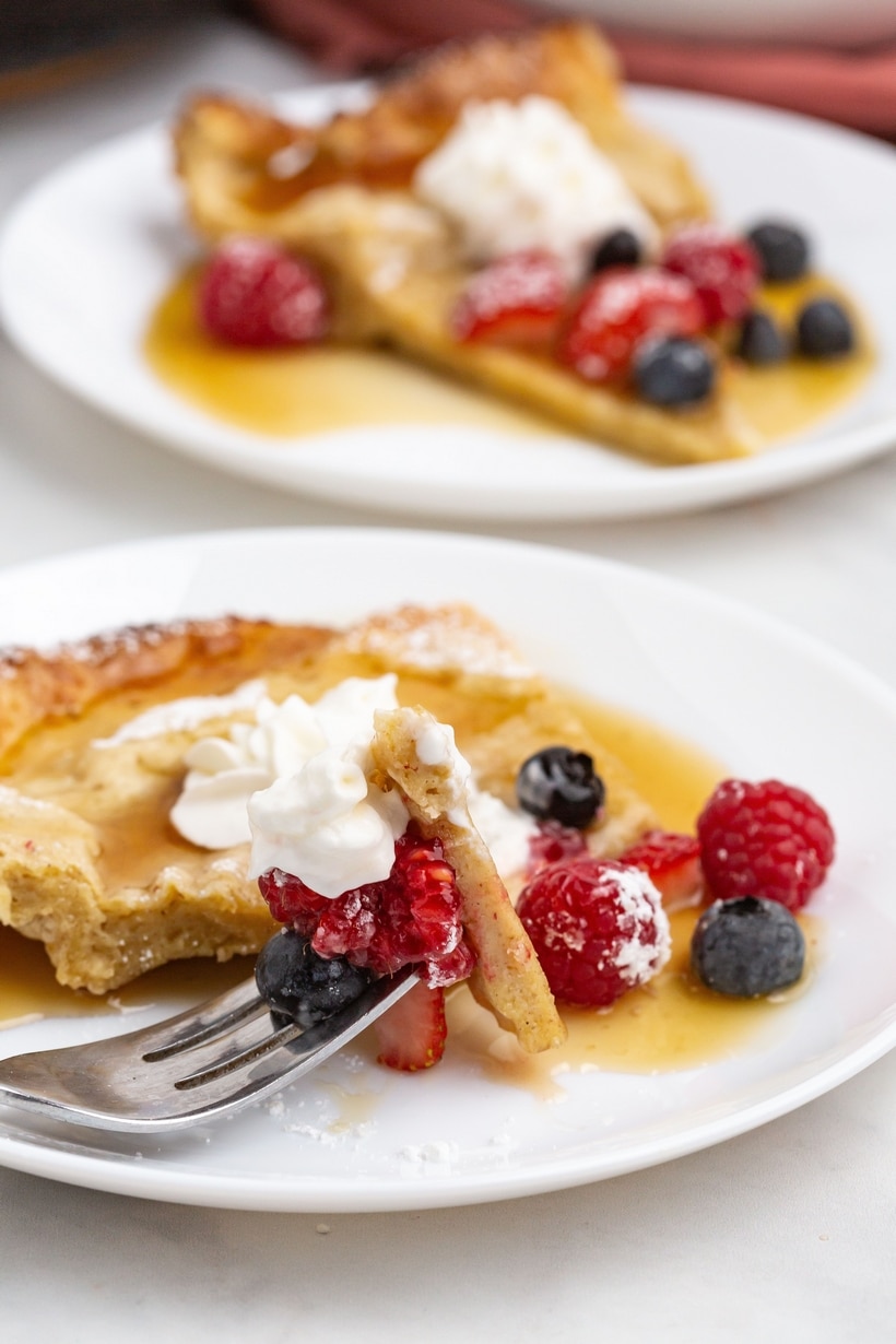 Two slices of extra billowy Dutch baby pancake on a plate with fresh berries 