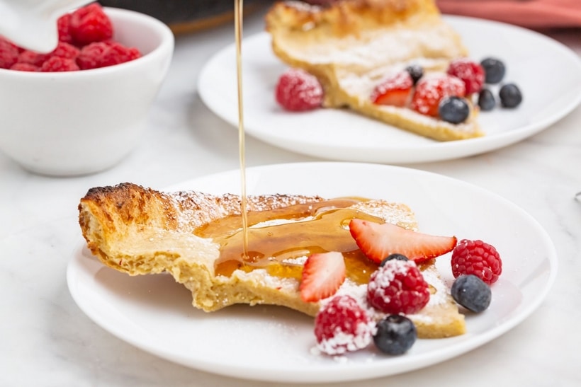 Slice of Dutch baby pancake recipe topped with berries and syrup
