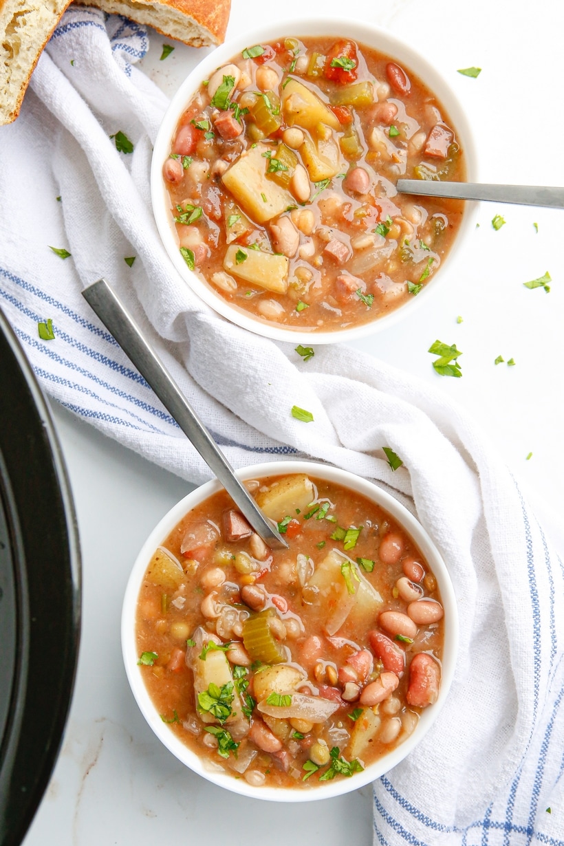 Overhead view of two bowls of ham and bean soup, each with a spoon tucked in, ready to serve.