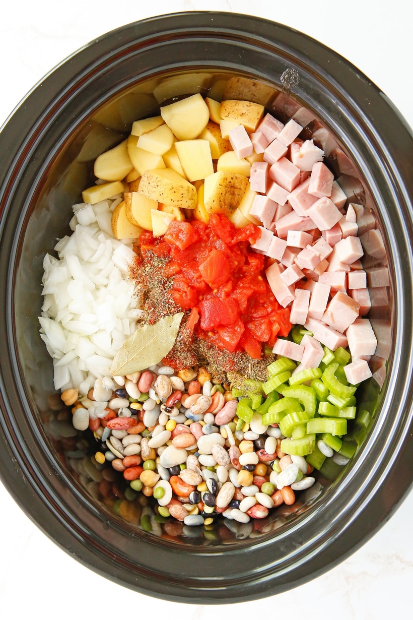 Overhead view of the slow cooker filled with uncooked beans, ham, and chopped vegetables before cooking.