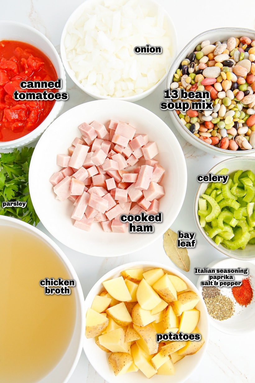All soup ingredients laid out on a surface, including beans, diced ham, vegetables, broth, and seasonings.