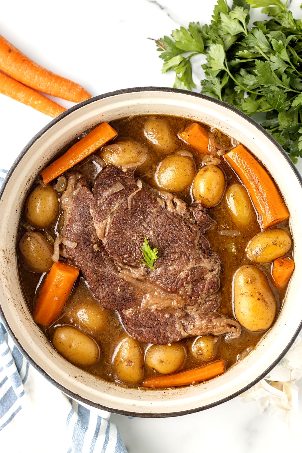 Stovetop pot roast with potatoes and carrots in Dutch oven Beef pot roast with carrots and potatoes simmering in rich gravy on the stove top
