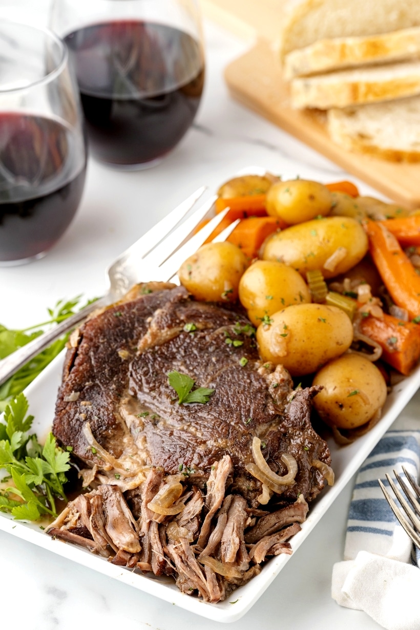 Shredded beef pot roast with gravy and vegetables Juicy stovetop pot roast pulled apart into pieces on a serving plate.