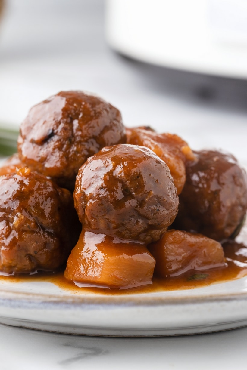 Click to see how to make these sweet and savory Hawaiian meatballs in a slow cooker. A serving of Slow Cooker Hawaiian Meatballs garnished with scallions, showcasing their sweet and savory pineapple glaze.