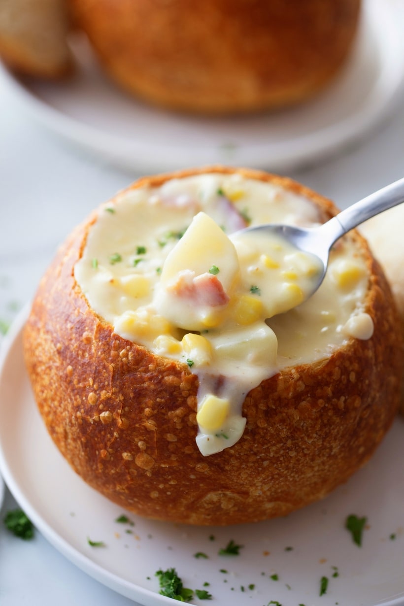 Corn chowder served in a sourdough bowl Corn chowder in a sourdough bowl with a spoon taking a serving.