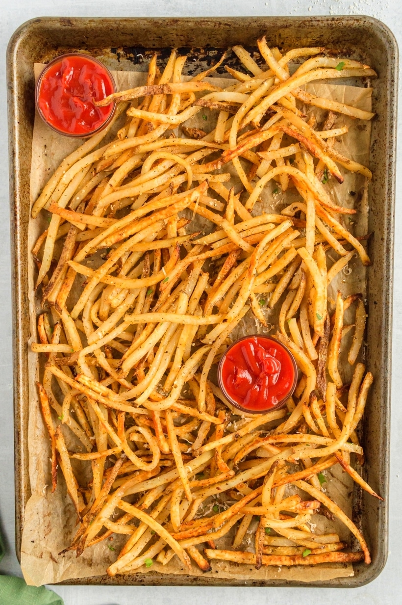 Baked French Fries (Oven Fries) with ketchup. Seasoned fries arranged in a single layer on a parchment-lined baking sheet, ready to bake.