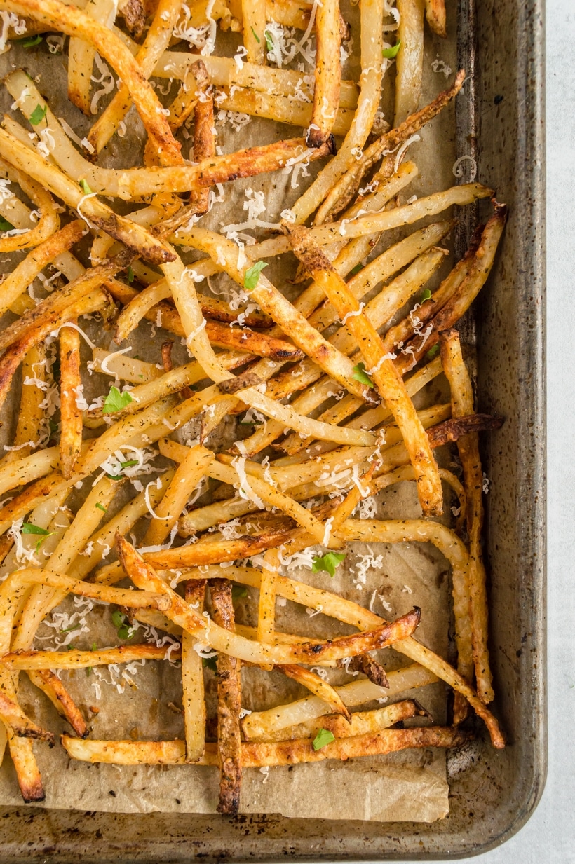 Baked French Fries (Oven Fries) on parchment paper. Close-up of seasoned fries on a baking sheet, coated with garlic olive oil and spices