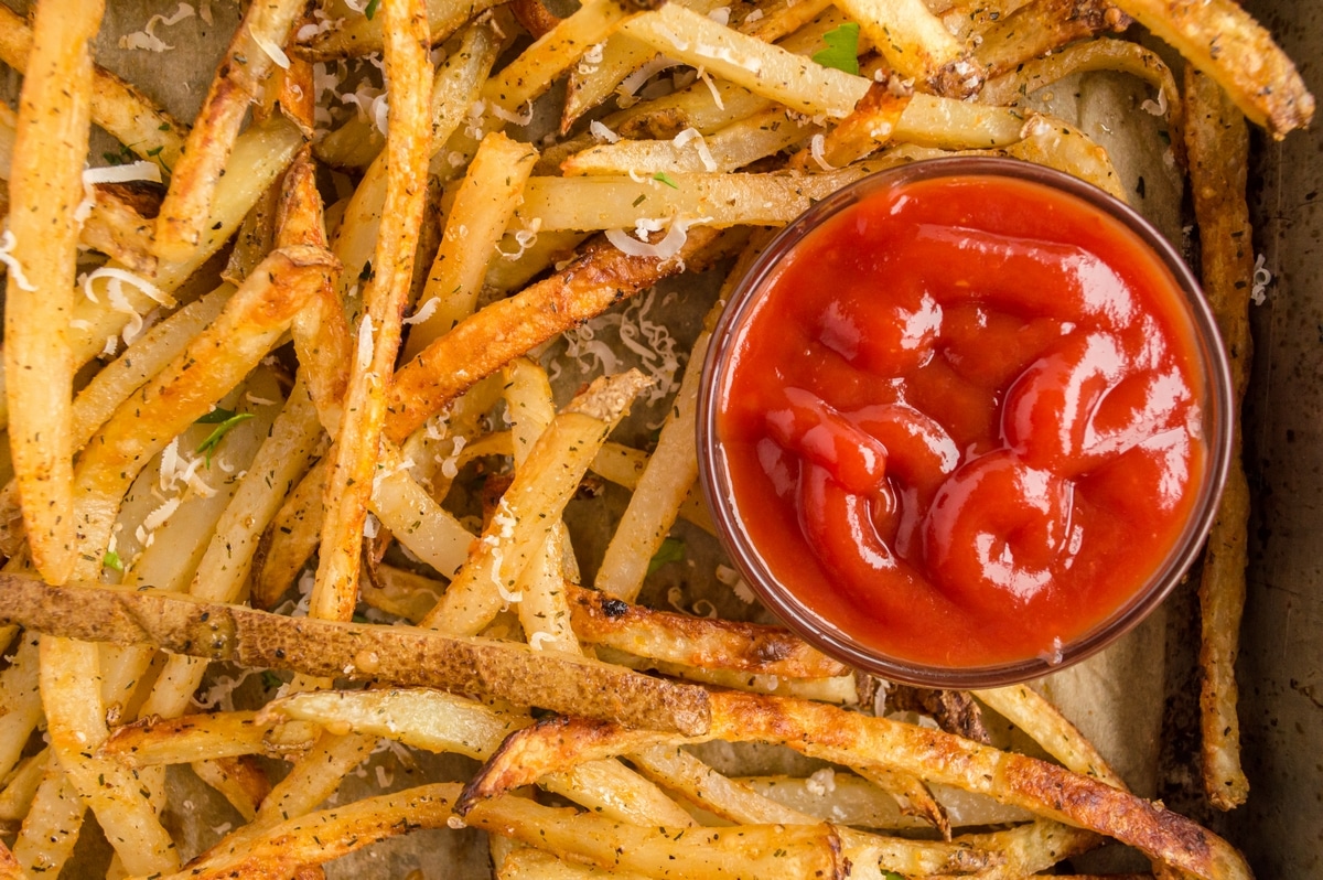 Baked French Fries (Oven Fries) on a baking tray. Garlic-infused olive oil drizzled over fries before seasoning and baking.