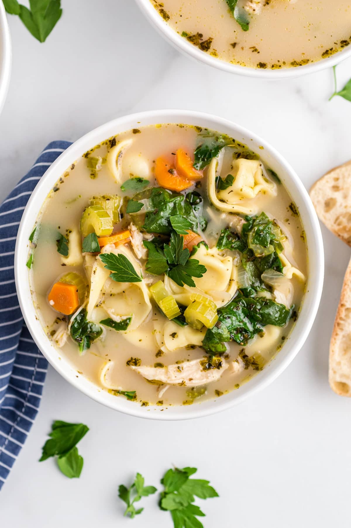 A bowl of chicken tortellini soup with cheese tortellini, shredded chicken, carrots, celery, spinach, and parsley in a light broth.