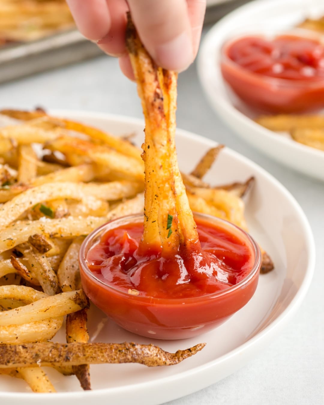 Baked French Fries (Oven Fries) being dipped in ketchup. Crispy Baked French Fries being dipped into ketchup for a perfect bite.