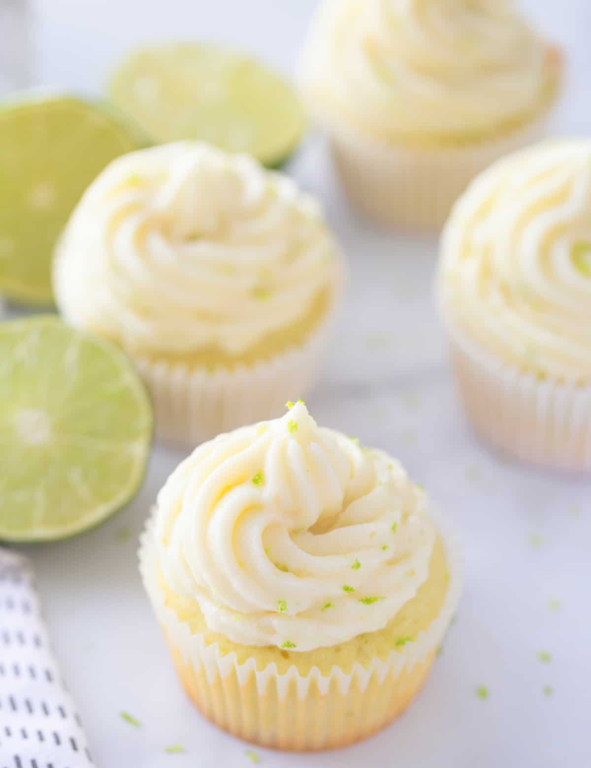 Key lime cupcakes cooling on a counter with frosting and lime zest on top 