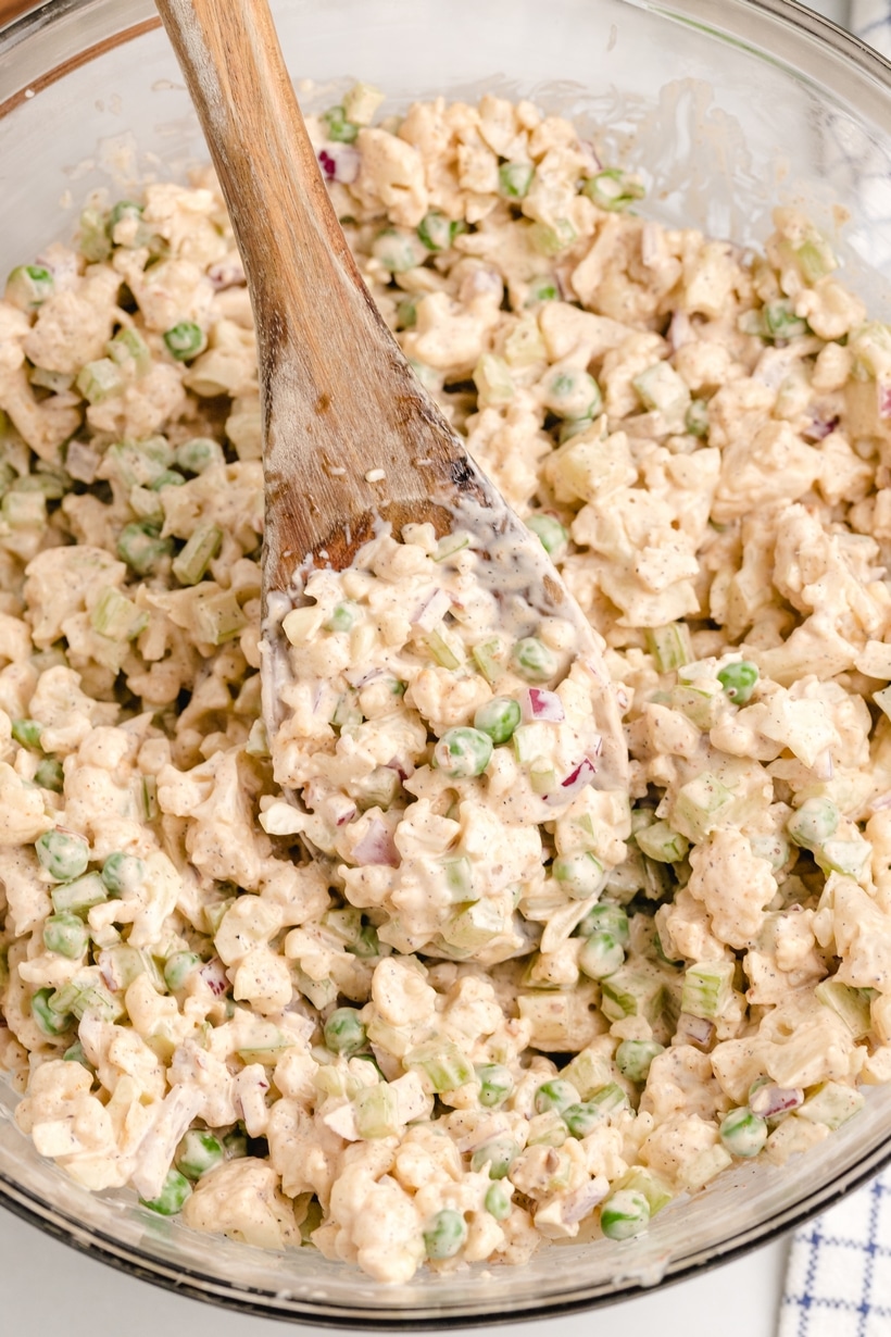 Creamy cauliflower salad in a bowl with wooden spoon Overhead view of creamy cauliflower salad in a clear bowl with a wooden spoon