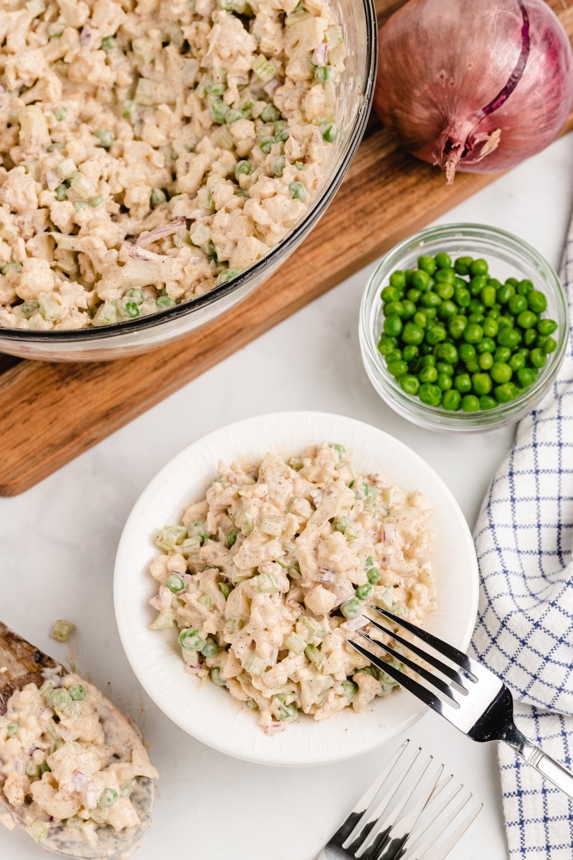 Serving of cauliflower salad with peas on the side Overhead view of a serving bowl of cauliflower salad next to a bowl of peas