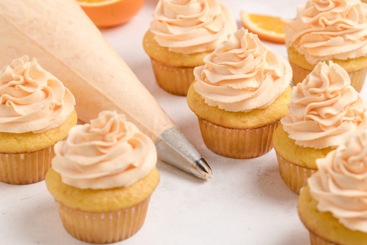 Frosted orange cupcakes with a piping bag filled with whipped orange frosting, ready to add the finishing touches.