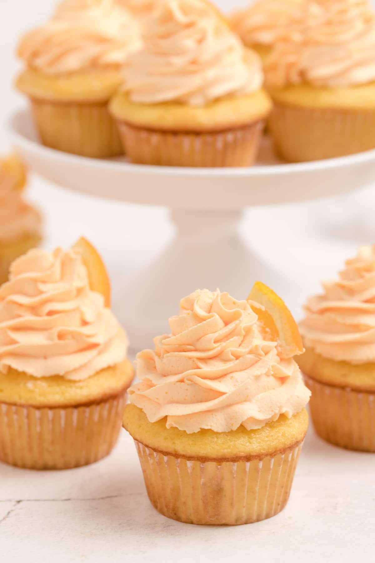 A close-up of a single cupcake with piped frosting, with a cake stand full of cupcakes slightly blurred in the background.