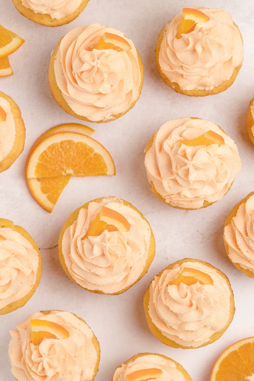 A top-down view of frosted orange cupcakes garnished with orange slices, highlighting their bright color and fluffy texture.