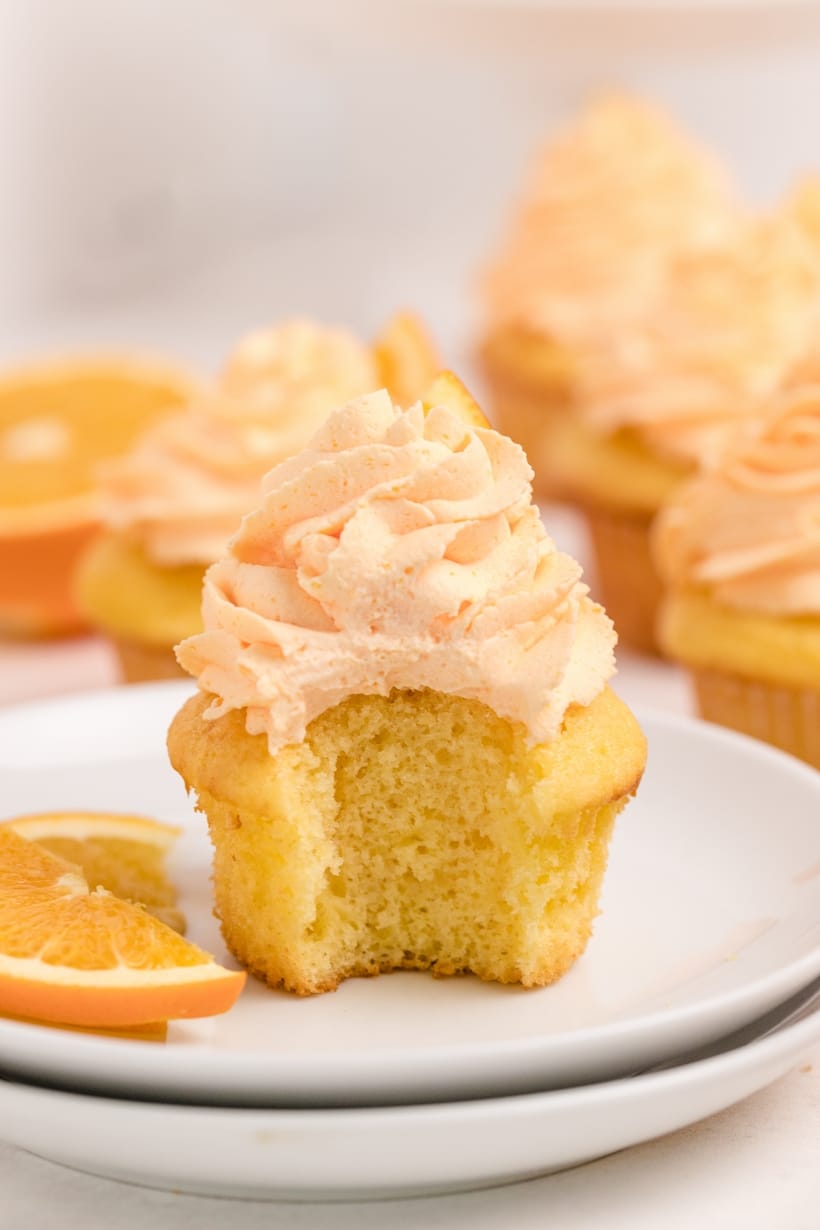 A single Dreamy Orange Cupcake on a plate with a bite taken out, showing its soft texture and creamy whipped orange frosting.