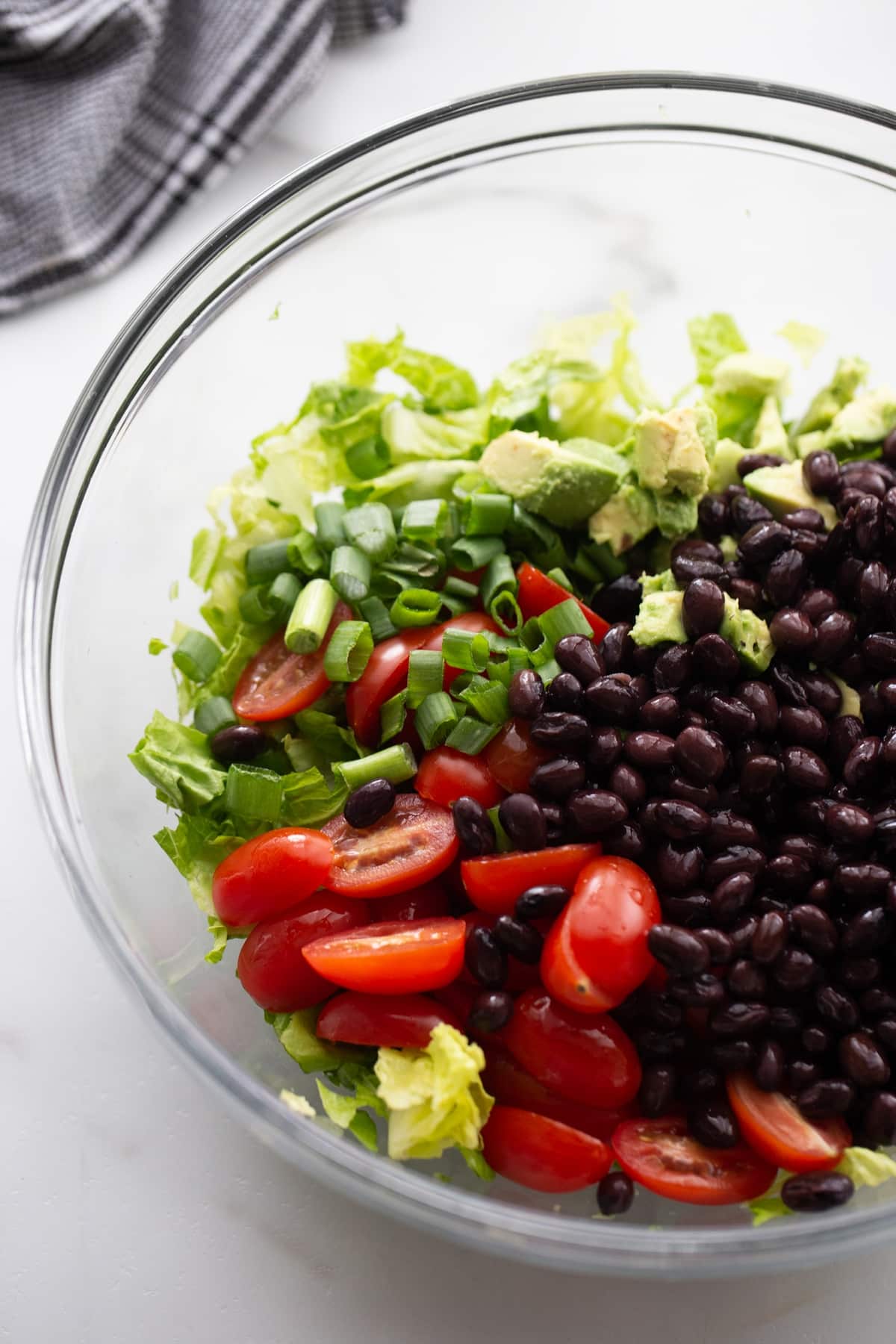 Shrimp and Avocado Taco Salad being prepared ingredients such as black beans, tomato, avocado in a bowl
