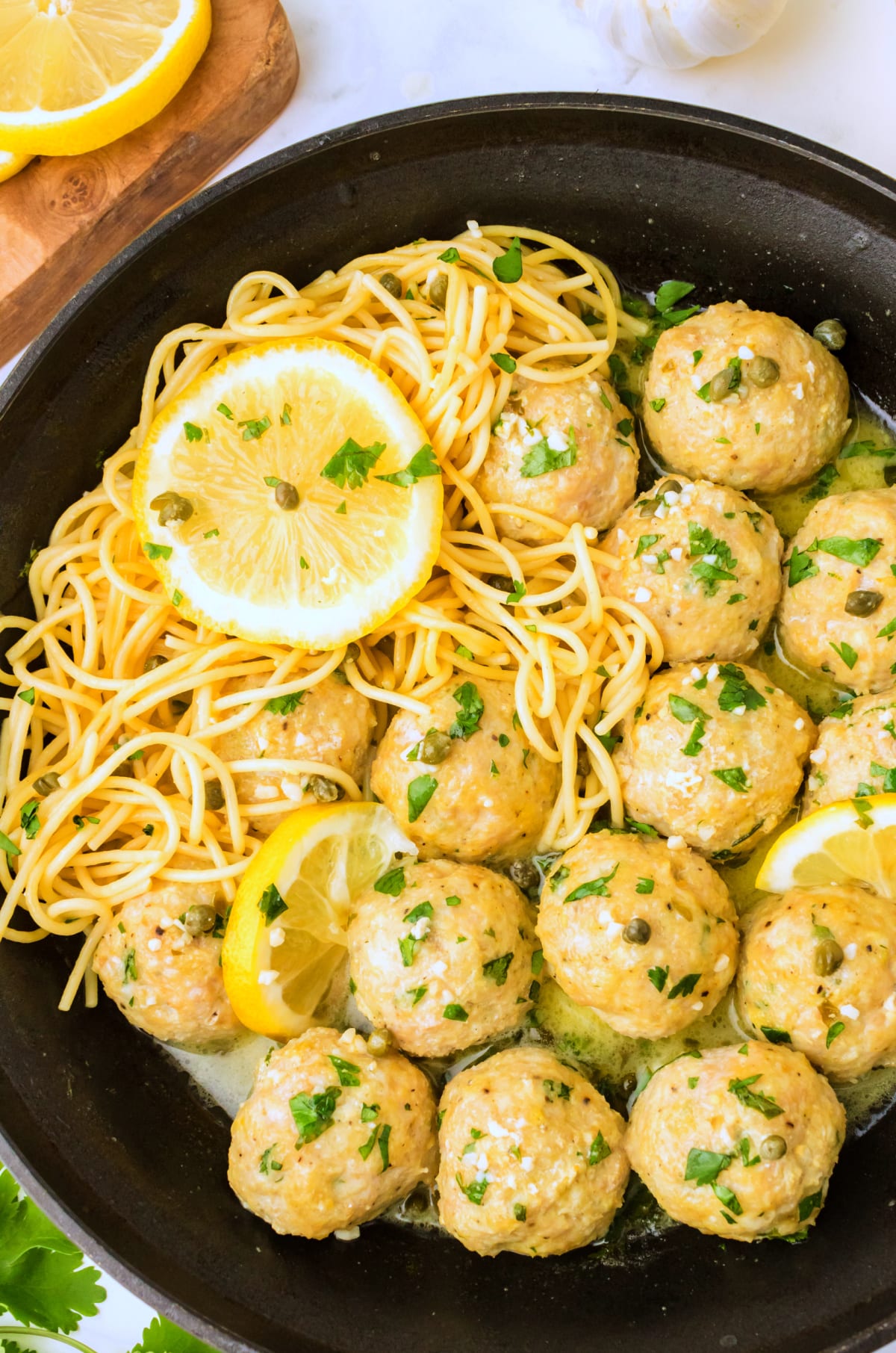 Chicken piccata meatballs in skillet with sliced lemon and capers, overhead view