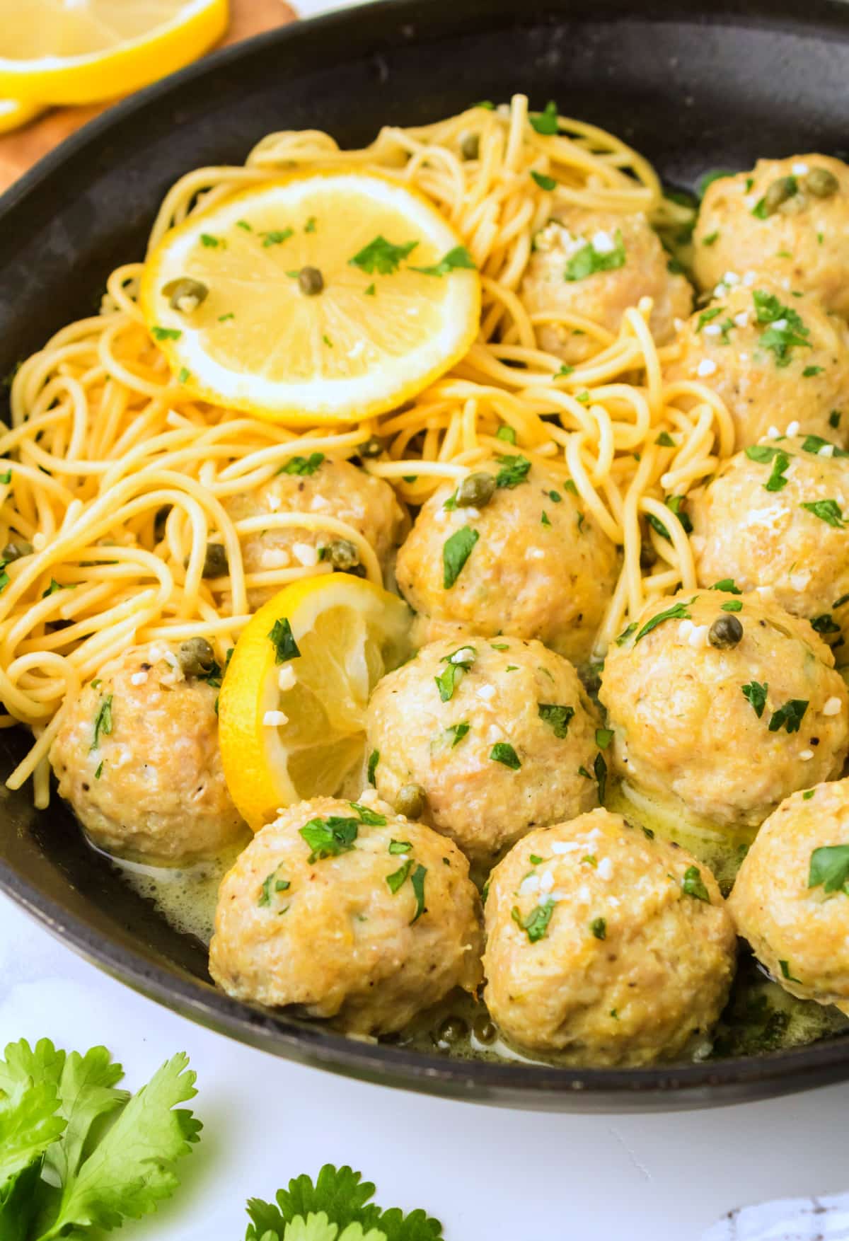 Baked chicken piccata meatballs in a skillet with pasta and lemon slices, side view