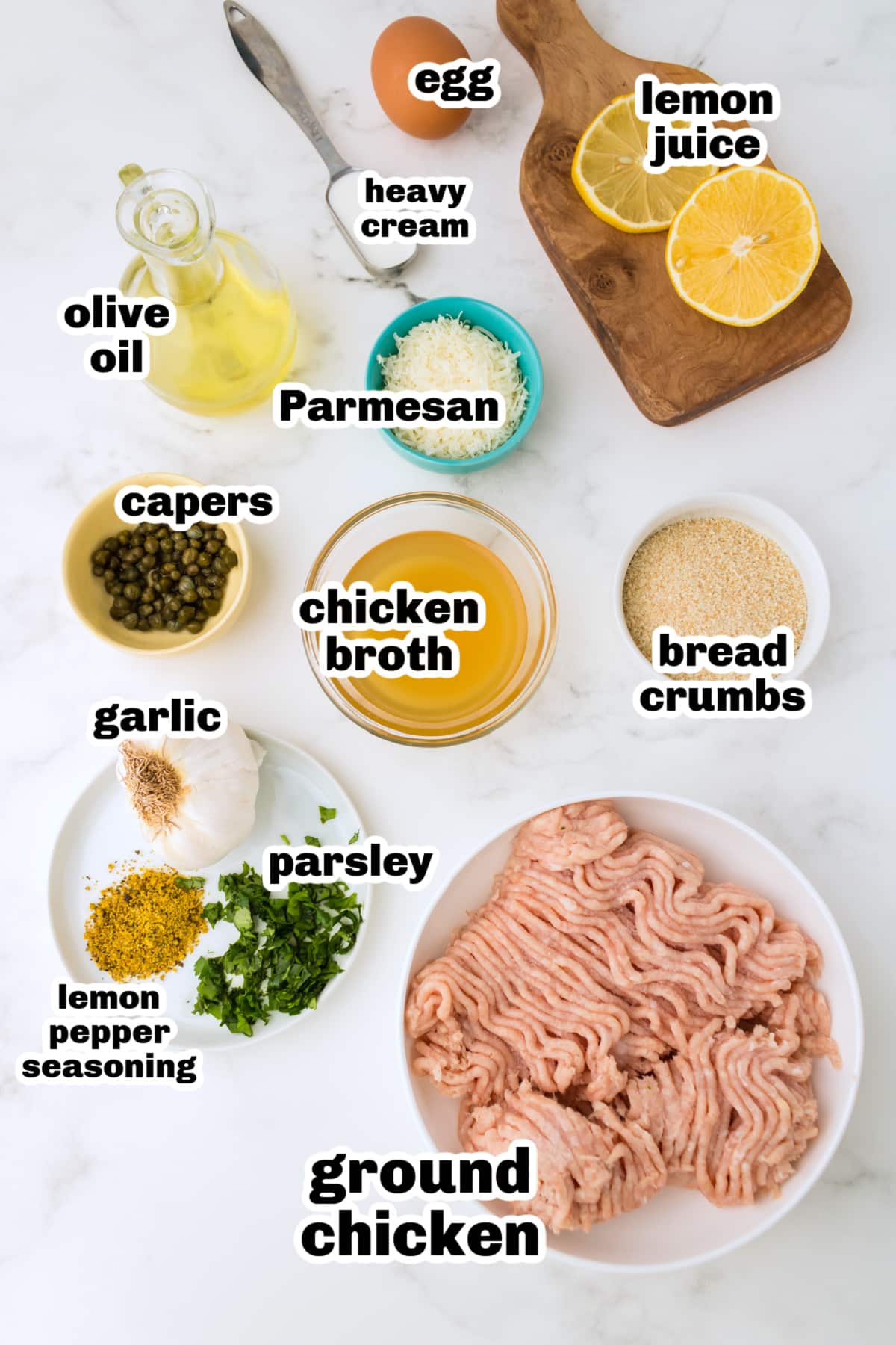 Ingredients for chicken piccata meatballs arranged on a surface with lemon, capers, and ground chicken