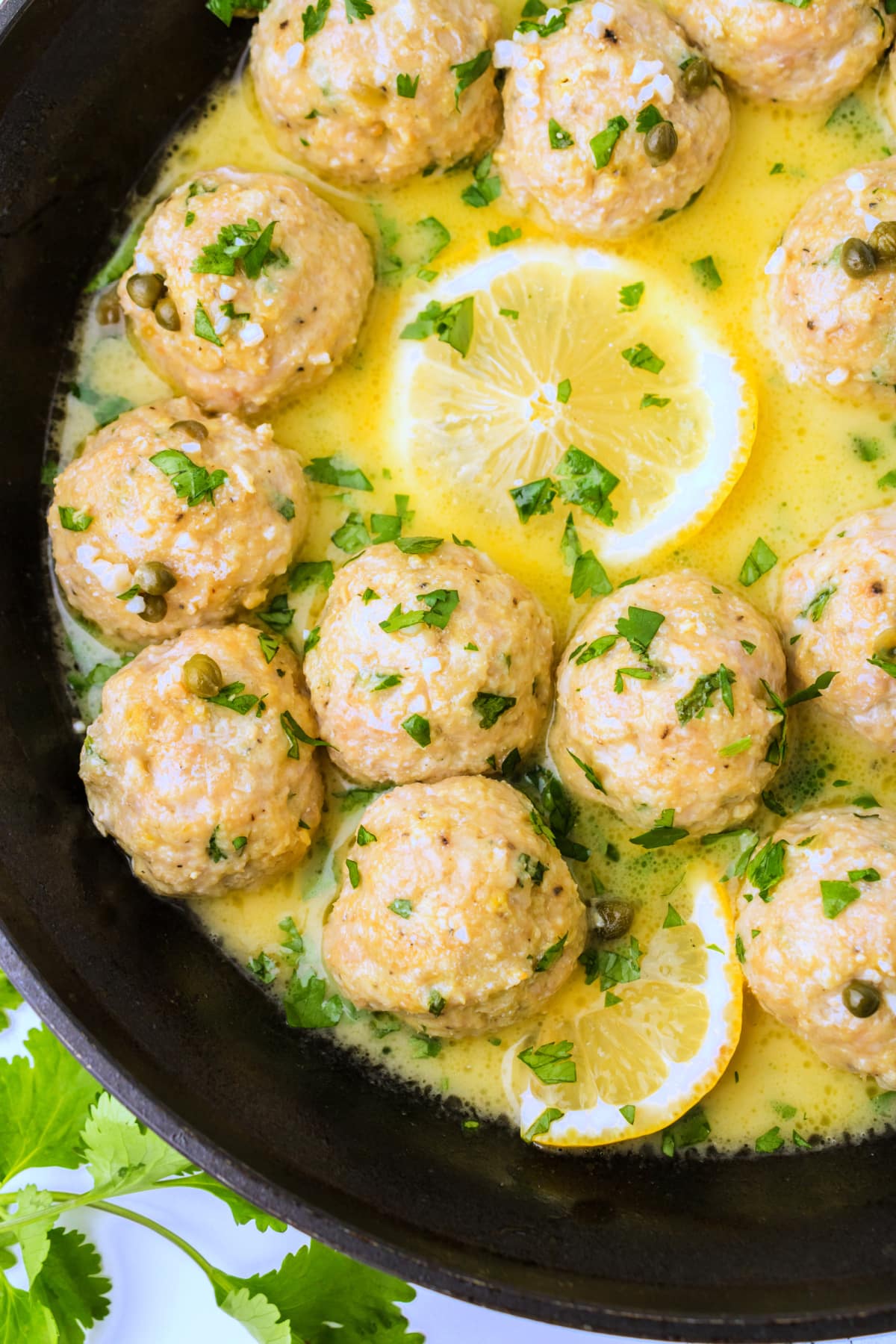 Closeup overhead shot of chicken piccata meatballs in skillet coated in lemon butter sauce 