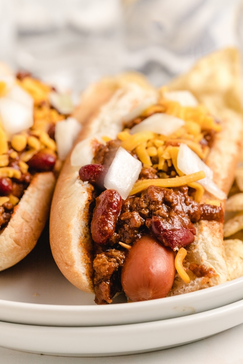Close-up of two chili dogs topped with cheese and onions on a white plate